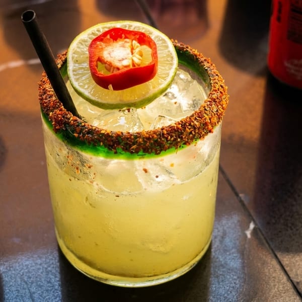 A vibrant margarita with a chili-lime rim, garnished with a lime slice and red chili.