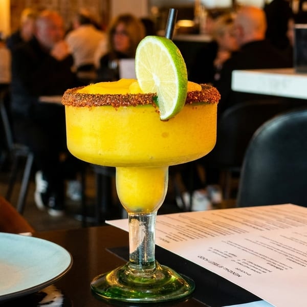 A mango margarita with a lime wedge and chili-salt rim sits on a table with a menu.