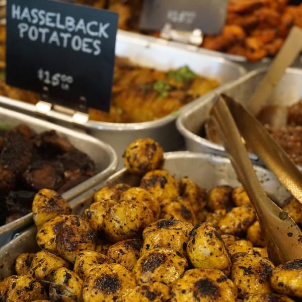 Close-up of golden Hasselback potatoes with charred tops in a metal serving tray at a buffet.