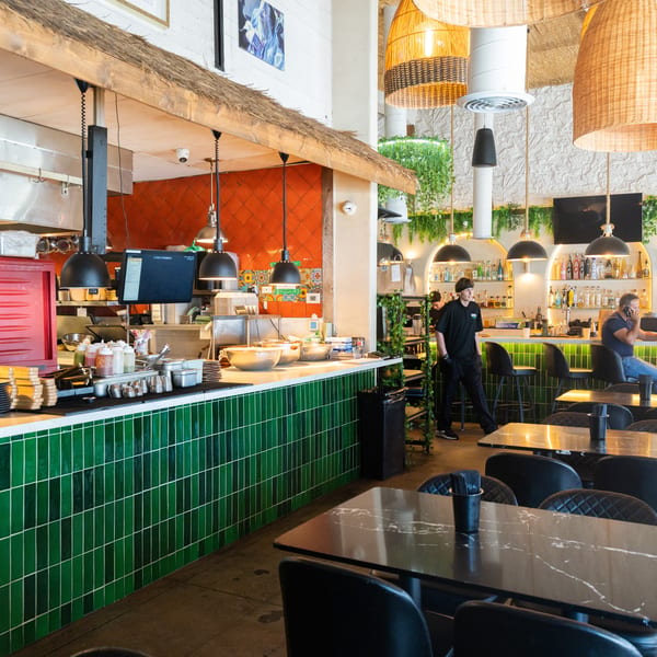 Restaurant interior with a green tiled counter, bar seating, and dining tables, with staff and customers.