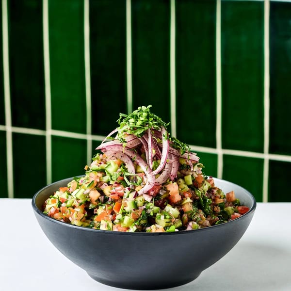 A vibrant chopped salad with tomatoes, cucumbers, and herbs, topped with red onion, in a black bowl.