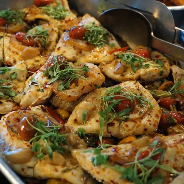 Close-up of baked chicken pieces topped with cherry tomatoes, onions, and fresh herbs in a serving tray.